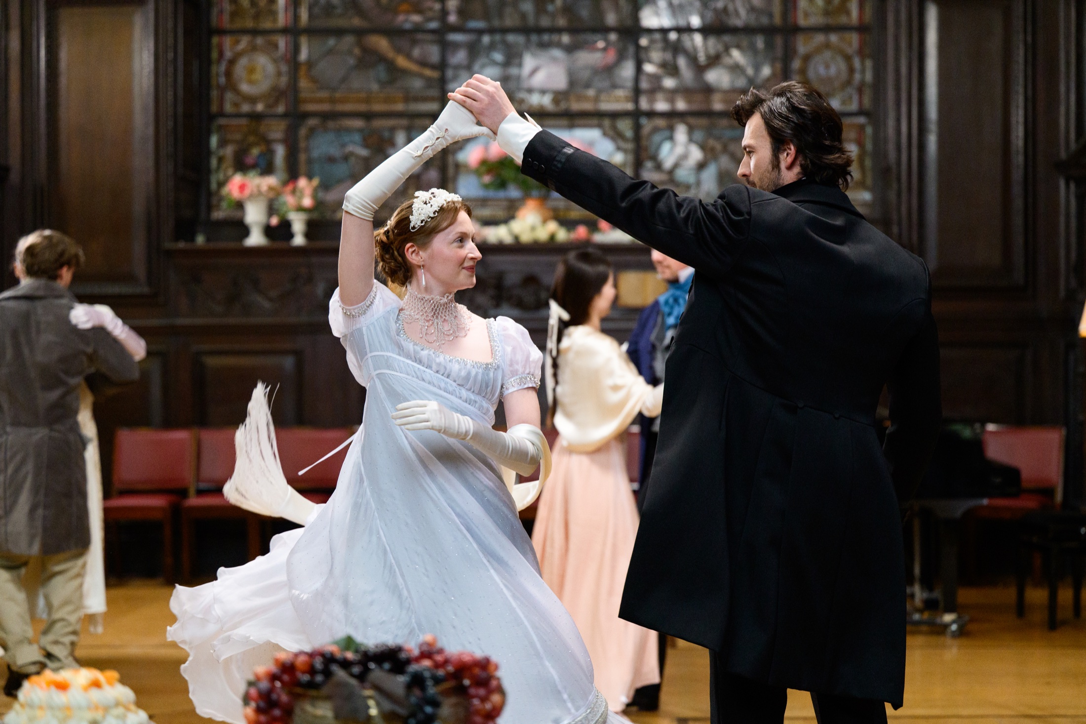 Period drama characters dancing in a wood-panelled room